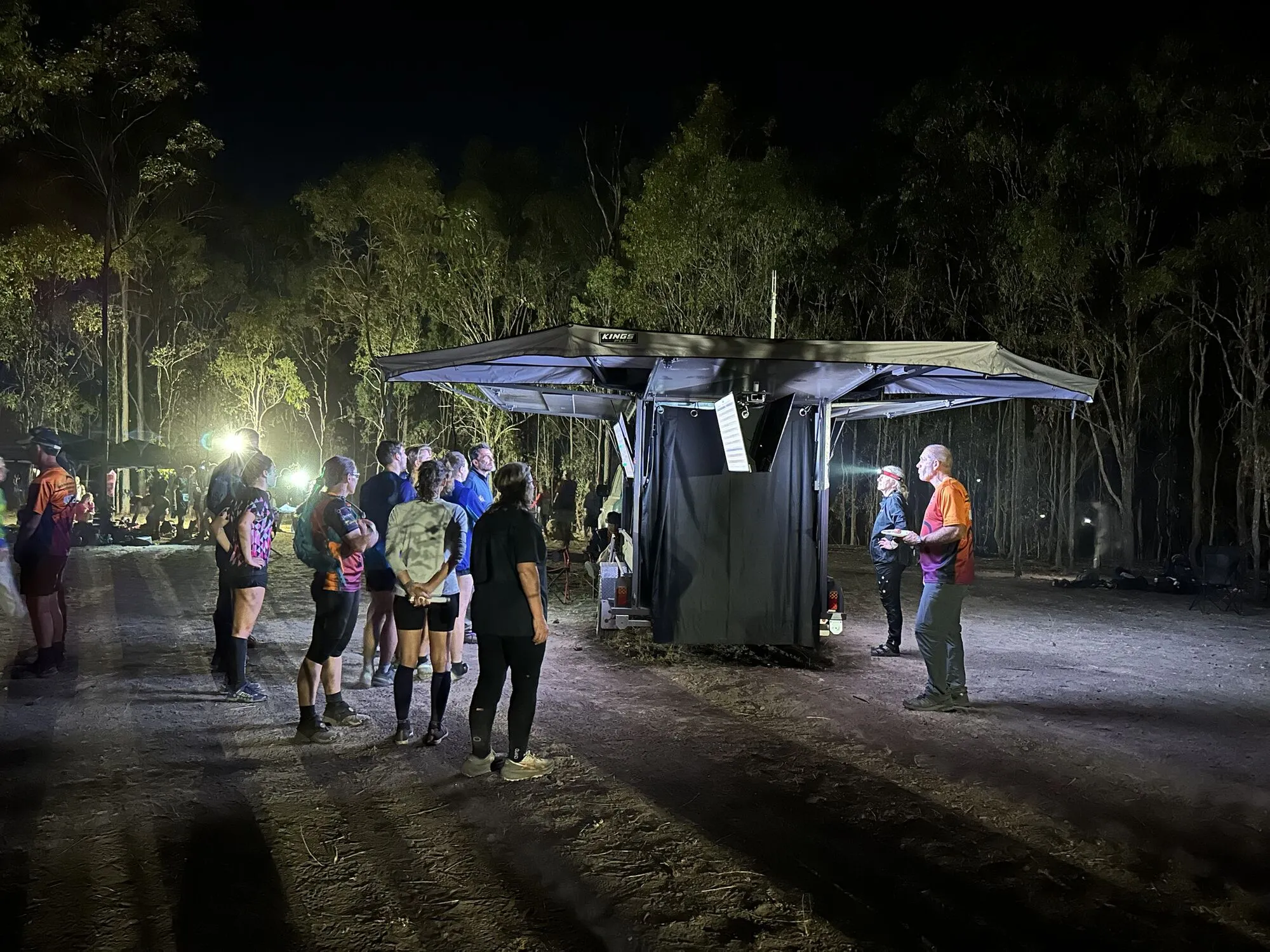 Competitors with head torches gathered at the lit results trailer in the bush after dark