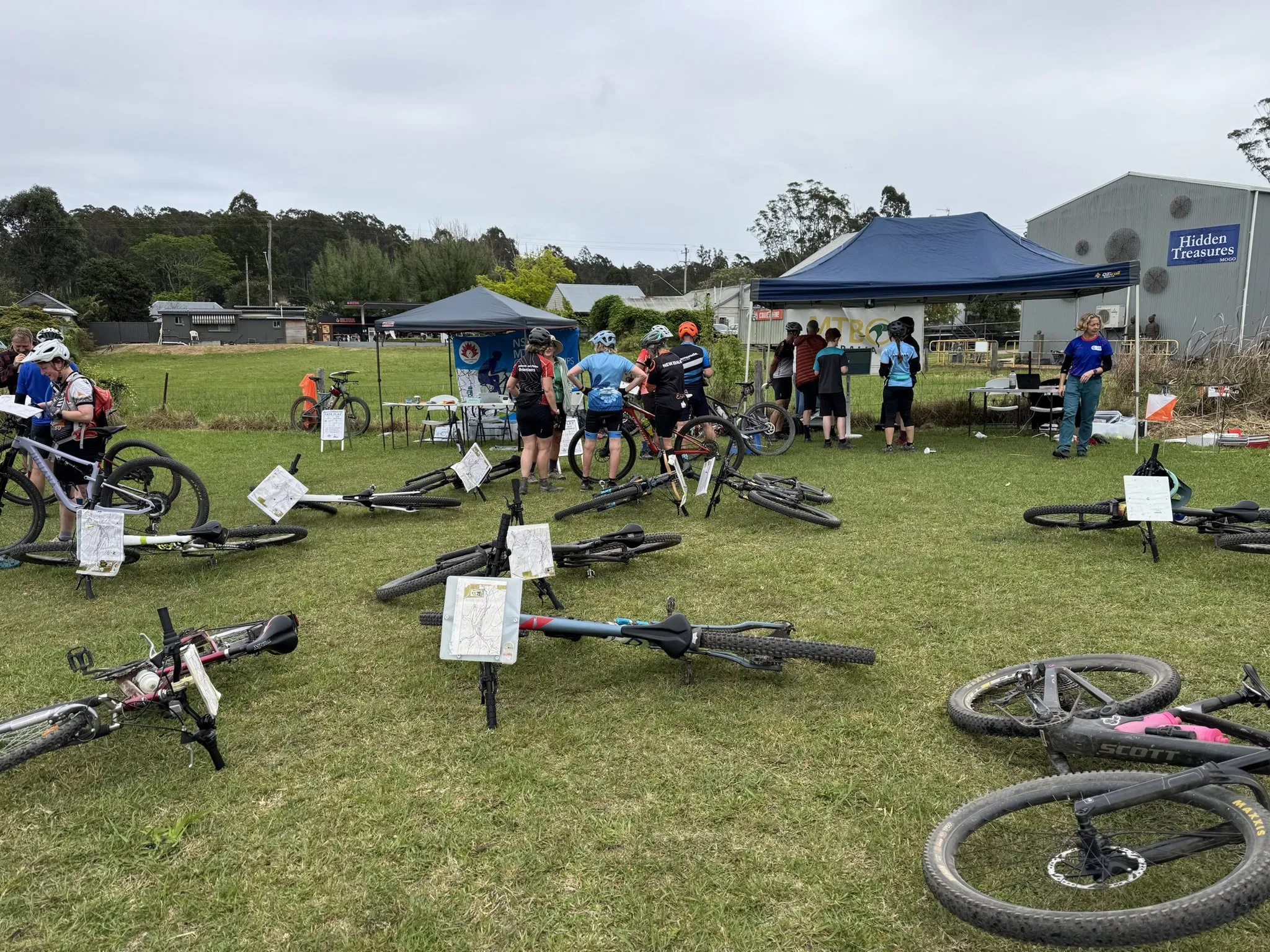 Mountain bikes with map boards lying on the grass in front of the NSW MTBO Championships and MTBO Australia marquees