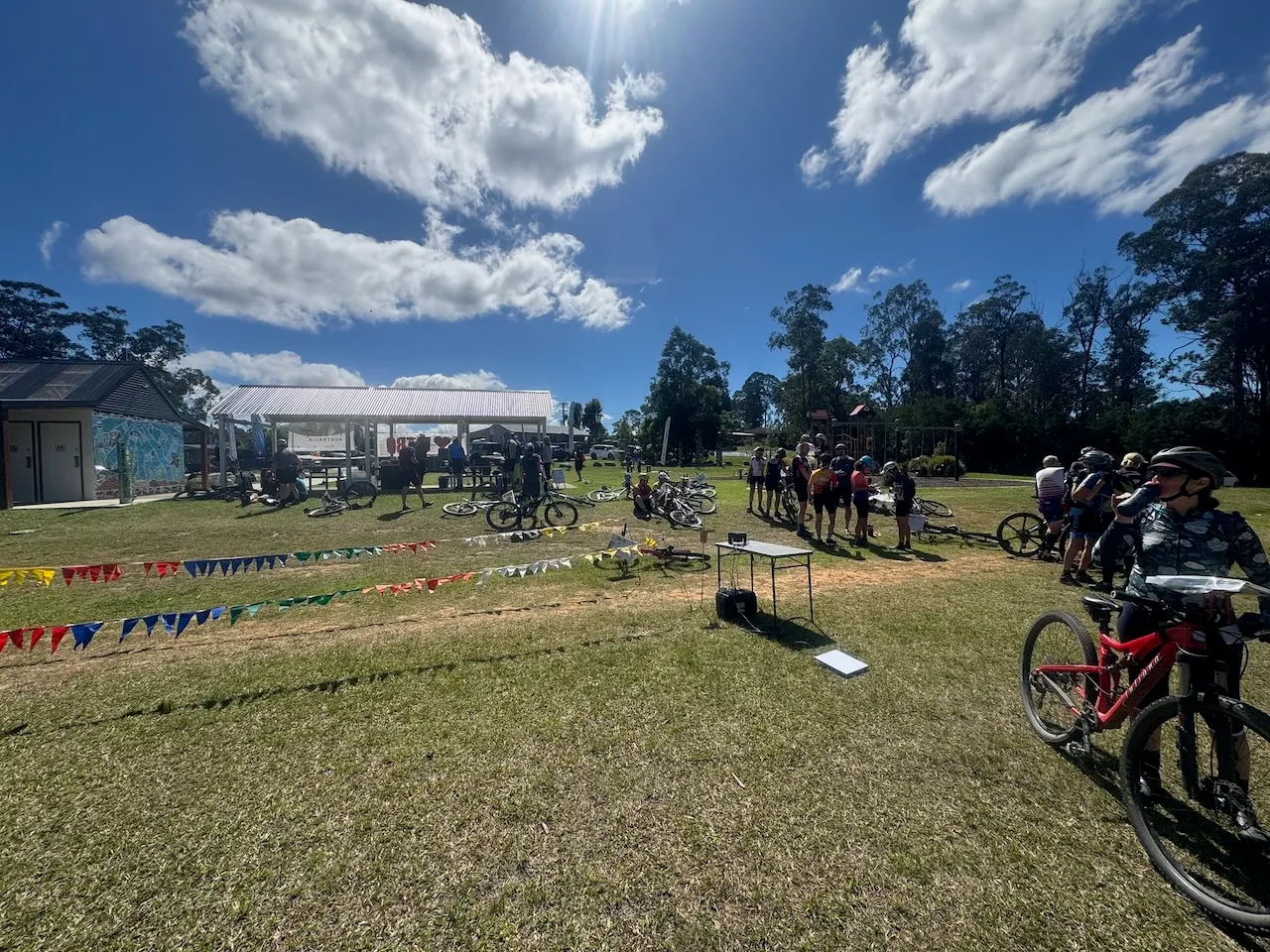 A rider in a green and white jersey leans over his bike to put his card in the download unit on a table at the finish, with bunting lining the finish chute behind