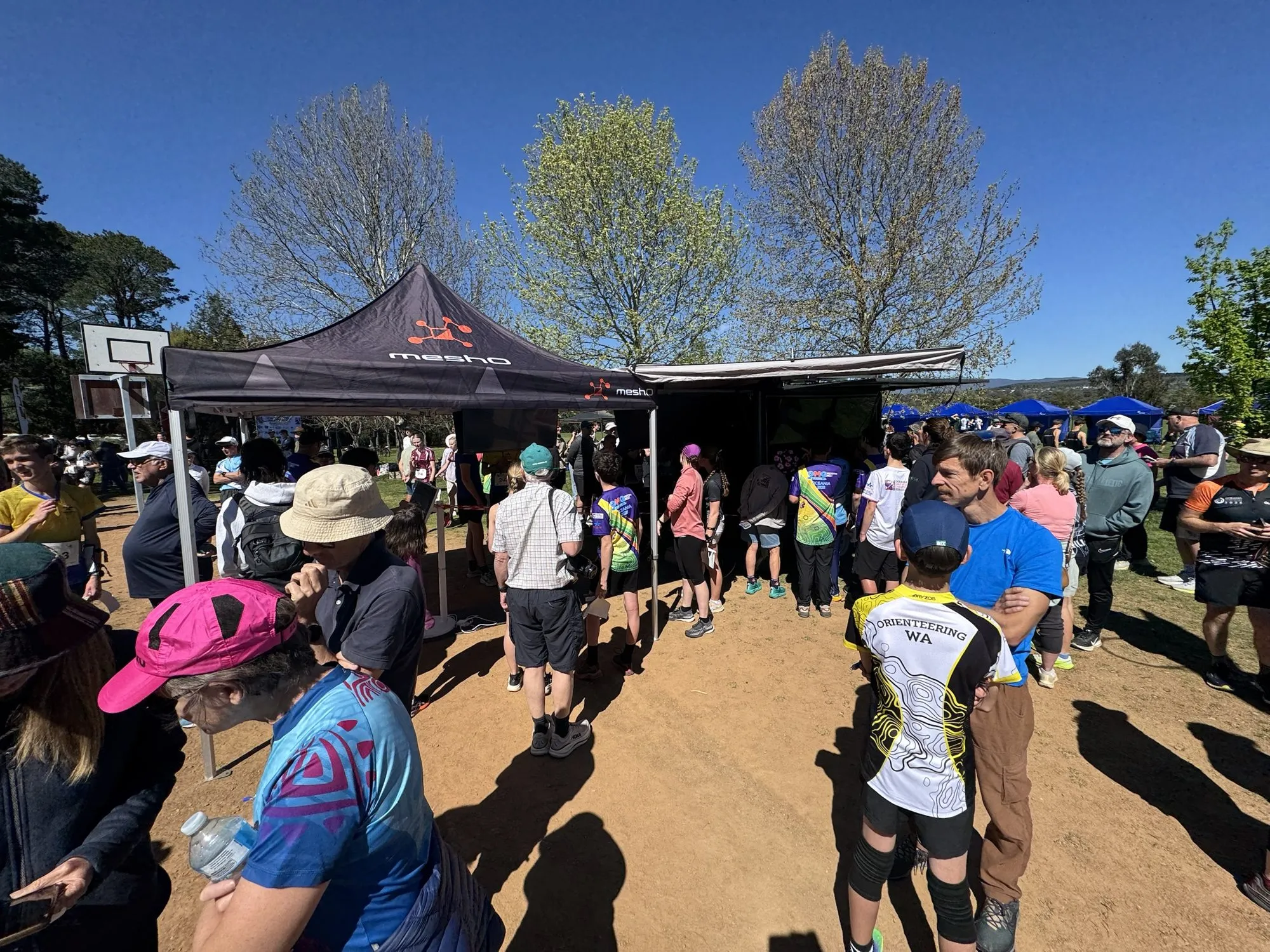 Competitors queueing under the meshO marquee and trailer awning on a school ground