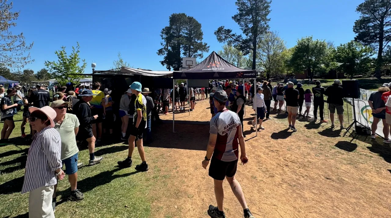 Competitors and spectators around the finish tents on a dusty track under gum trees, one runner walking away from the tents in the foreground