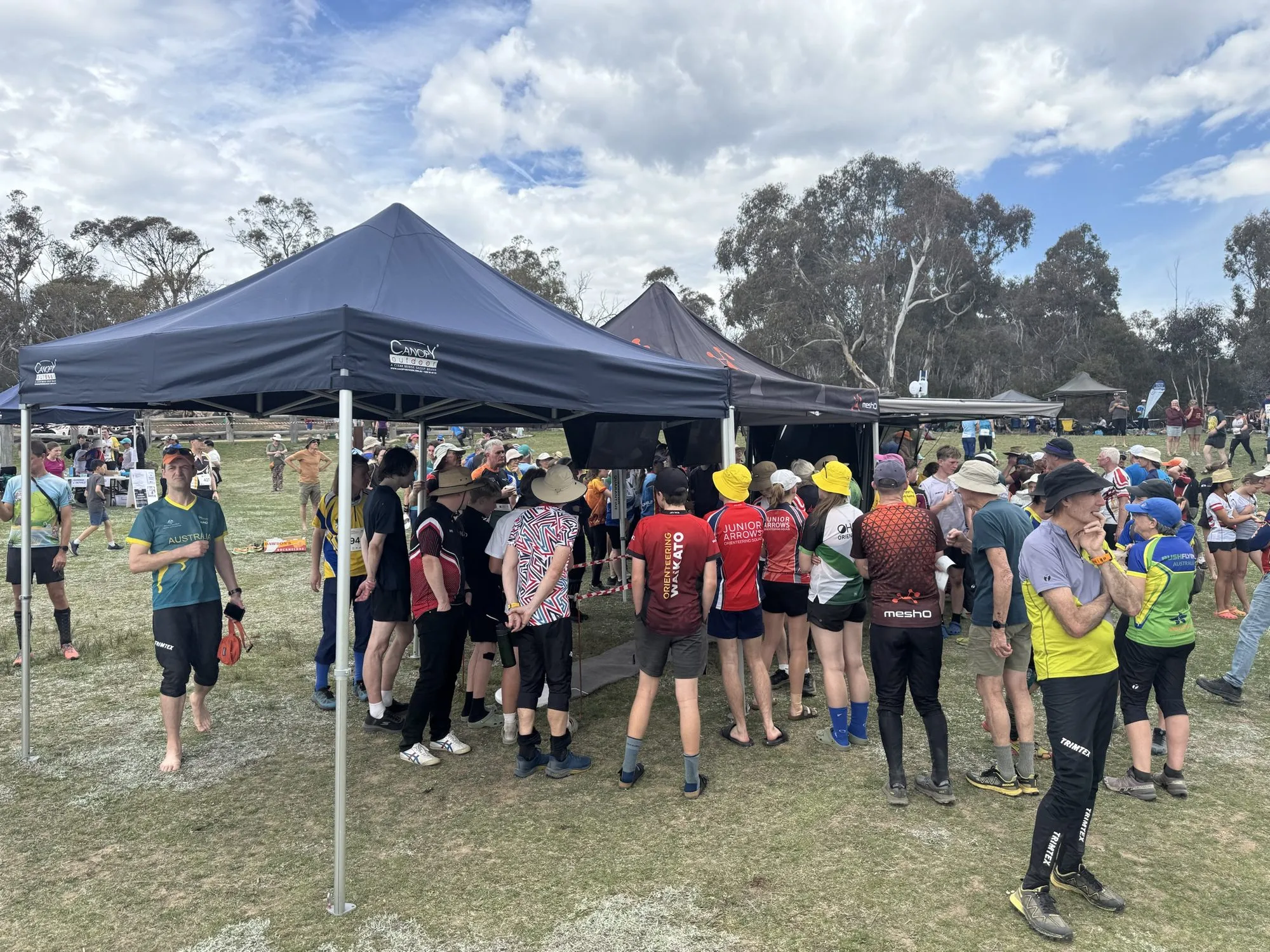 Competitors in club tops crowding under meshO marquees to read the results screens